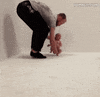 Video gif. A newborn baby, held upright by an adult, eyes wide open in alarm, shuffles their feet across the floor very fast, running with assistance. 