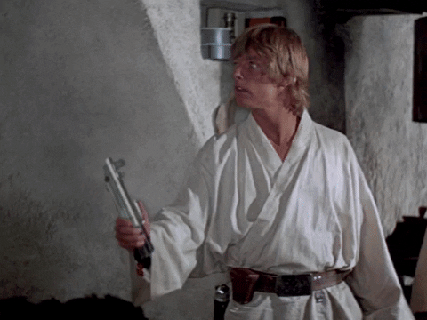 Star Wars gif. Mark Hamill as Luke Skywalker in Star Wars: Return of the Jedi holds a blue lightsaber in his hand. He looks at the lightsaber in awe as it lights up and flashes back down. 