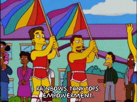 The Simpsons gif. Crowd of gay men and women and drag queens hold hands and wave, walking in a pride parade. Milhouse rides on a buff speedo-wearing man's shoulders. Text "Rainbows. Tank tops. Empowerment."