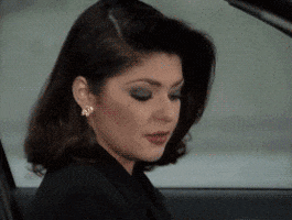 Video gif. Ready to leave, a woman in a car looks around and slowly rolls up her window.