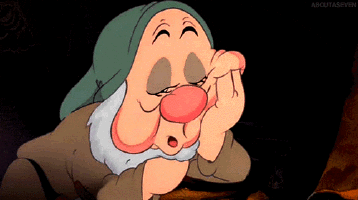 Disney gif. Sleepy from Snow White and the Seven Dwarfs rests his face on his hand as he struggles to keep his eyes open, before falling asleep in his arms.