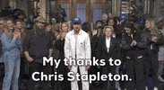 Video gif. Saturday Night Live castmember Mikey Day and guest host Ryan Gosling are dressed as Beavis and Butt-head for a sketch. Day and Gosling are sitting in the front row of a talk show audience. The two of them are staring straight ahead with goofy smiles on their faces. 