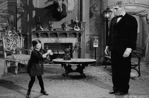 TV gif. Black and white video of a little girl with braids from the '60s The Munsters show tap dances while a formally-dressed Herman Munster looks on.