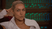 Reality TV gif. Blonde contestant on The Bachelor with her fingers behind her head and her eyes darting left and light, pondering or scheming.