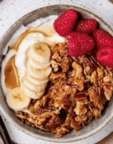 Spoon lifting granola from a bowl of thick yogurt topped with banana slices and raspberries