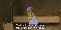 Disney gif. Winnie the Pooh stands in his all-brown bedroom, dressed in vibrant indigo pajamas with a purple nightcap and a dark blue sleeping mask. He pats the top of his belly hungrily and says, 