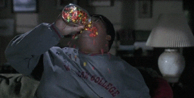 Movie gif. Eddie Murphy as Sherman Klump in The Nutty professor pours a whole jar of jelly beans into his mouth like he’s trying to drown himself in it. The jelly beans spill out of his mouth and roll down his chest and onto the ground.