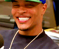 Celebrity gif. T.I. smiles, spinning slightly in his chair while on a podcast.