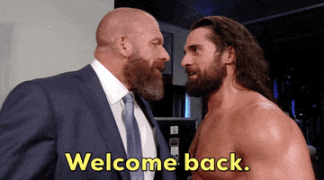 Celebrity gif. Seth Rollins stands shirtless eye to eye to a bald man in a suit. They stare intently at each other. The man in the suit slaps the man's bare chest and walks away. Yellow text reads, "Welcome back."