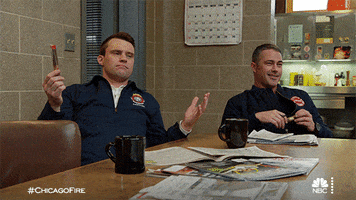 TV gif. Jesse Spencer as Matthew Casey on Chicago Fire and Taylor Kinney as Kelly Severide sit at a table together with coffee mugs and newspapers on the table in front of them. Matthew looks over at Kelly with his hands up as if to say, "Am I right?” Kelly looks at him laughing.