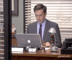 The Office gif. Ed Helms as Andy sits in his office and looks at his open Macbook. He lifts his hands up in tight fists, snarling and frowning with anger in reaction to something on screen.