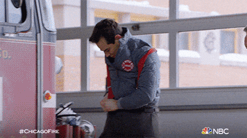 TV gif. Firefighters on Chicago Fire quickly get dressed in their gear as a woman firefighter watches and times them.