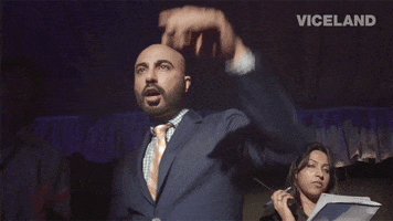 Video gif. A man in a suit says "go," and waves his arms with a flourish, on ViceLand. 