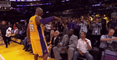 Sports gif. Kobe Bryant in his Lakers uniform goes over to Shaq who is sitting courtside and gives him a high five.