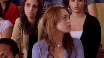 Movie gif. Sitting on bleacher seats with other students, Lindsay Lohan as Cady in Mean Girls looks to the side, raises her hand and waves her fingers.