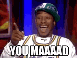 Video gif. Cam'ron wearing a sideways ball cap, chain, and a basketball jersey smiles and points at Bill O'Reilly offscreen. Text, "You mad"