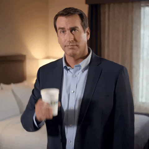 Ad gif. Actor Rob Riggle, in a commercial for Holiday Inn, lifts a branded cup of coffee in a hotel room as if to say, "Here's to you." Text, "Here's to you"