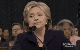 Political gif. Hillary Clinton sits in front of a microphone at a congressional hearing. She chuckles, looking away, and then props her head up with her hand. She looks up at the judges with an annoyed look on her face.