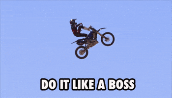 Sports gif. Motocross rider is in the midst of flying through the air and stands up on his bike, putting one foot on the handlebars. Text, "Do it like a boss."
