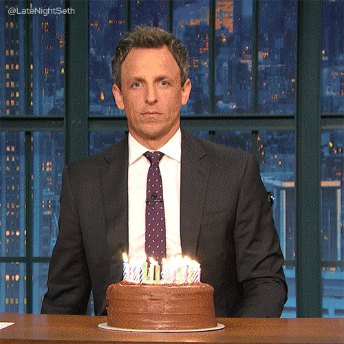 Late Night  gif. Seth Meyers sits at his desk with a birthday cake with many lit candles. He pulls a fire extinguisher out from under his desk and blasts the cake so the candles’ flames are put out. With a straight face, he looks at us and puts the fire extinguisher back under his desk.