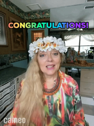 Celebrity gif. Carole Baskin wears a flower crown and a tie-dye sweatshirt, sitting in a kitchen as she says with a smile, "Congratulations!"