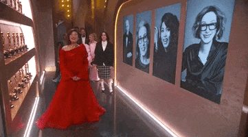 Oscars 2024 GIF. Ariana Grande, Cynthia Ervo, Billie Eilish, and Finneas try to scooch by a presenter backstage at the Oscars but are adorably obvious about it. Eilish leads the charge, doing a couple quick side steps in a failed attempt to not distract the camera or presenter.