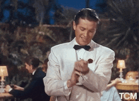 Movie gif. Robert Cummings as Jeffrey in Moon Over Miami wears a white tux as he checks his watch, then points assertively as if to give a cue.