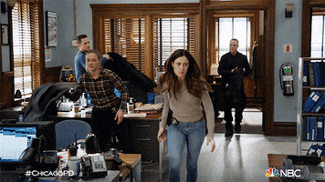 TV gif. Four officers on One Chicago grab their coats and slip them on as they hastily file out of an office. 