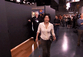 TV gif. Backstage behind the set in The Comeback, we see a woman walk past in front of Robert Michael Morris as Mickey who walks off smiling and giving us a thumbs up.  