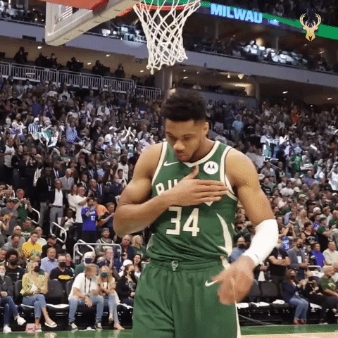 Sports gif. Giannis Antetokounmpo stands on the court in his Bucks uniform and looks up with his palms pressed together in prayer as he takes a breath.