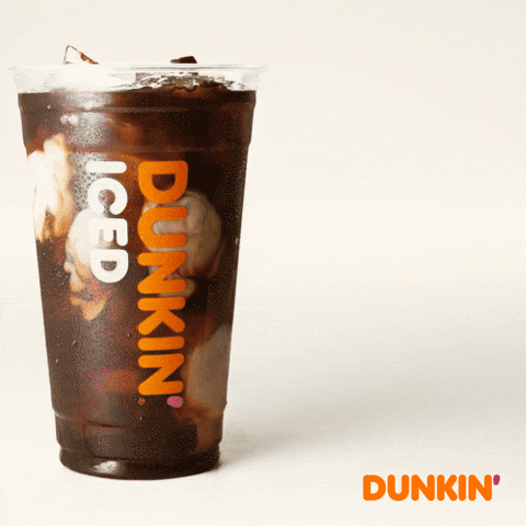 Sponsored gif. Cream swirls through a plastic cup of Dunkin’ Donuts iced coffee just before an orange straw is dropped into it. Text reads, “Wake up.”