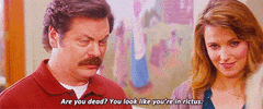 Parks and Recreation gif. Nick Offerman as Ron squints with suspicion while speaking, while Lucy Lawless as Diane looks on with a subtle smile. Text, "Are you dead? You look like you're in rictus."